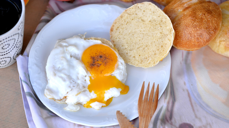 Fried egg on a bun on a plate with fork and coffee