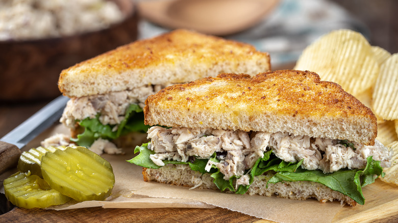 Tuna salad and lettuce on toasted bread with pickles and chips