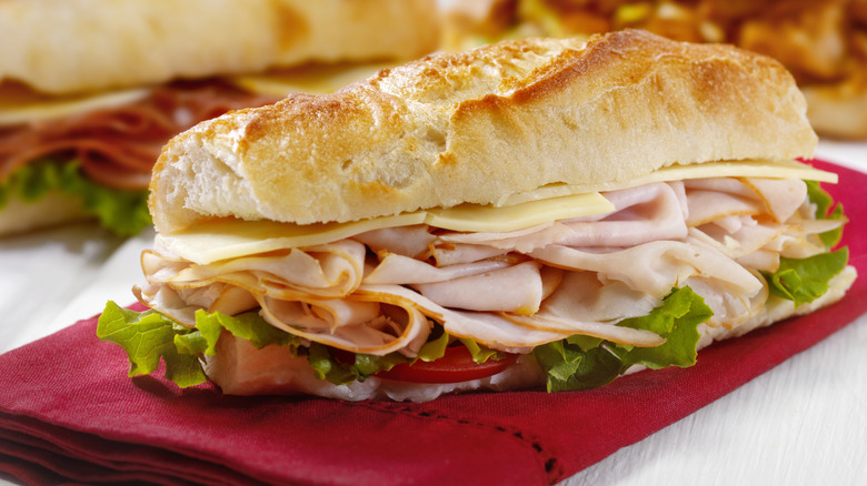 Sub sandwich on baguette bread with sliced meat, cheese, lettuce, and tomato on red napkin