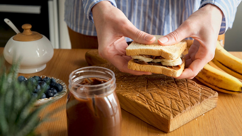 Hands holding a nutella and peanut butter sandwich over a cutting board