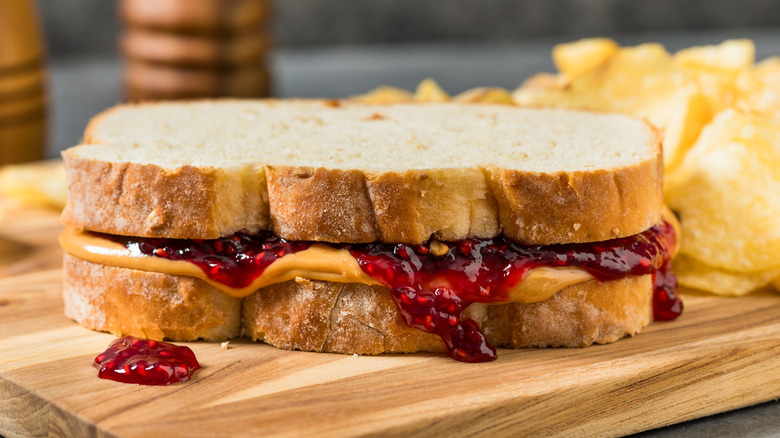 Peanut butter and jelly sandwich on wooden board with chips