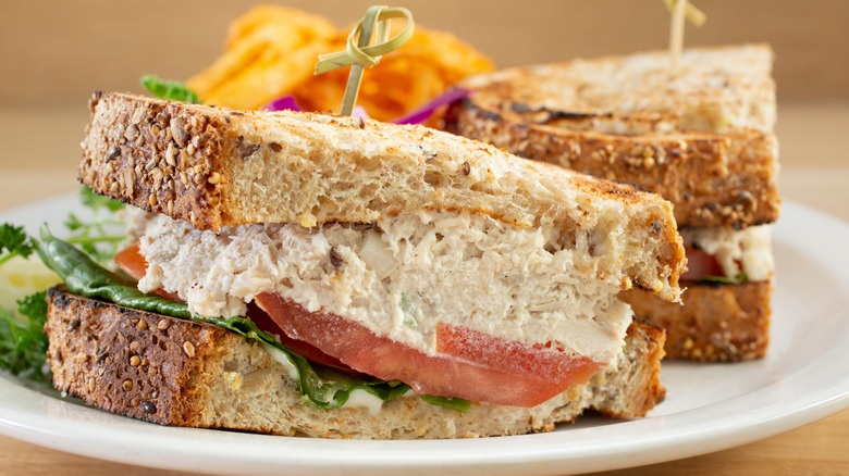 Tuna salad sandwich with tomatoes, lettuce, and sandwich picks on plate