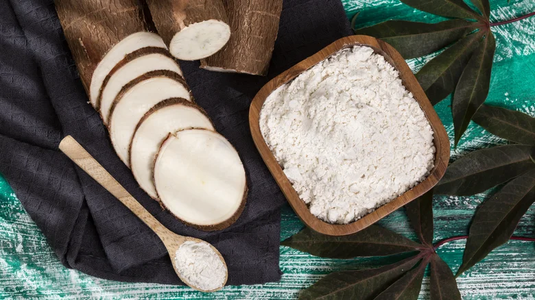 Raw cassava root and flour on navy cloth by leaves