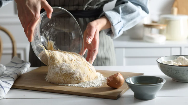 Person pours raw dough ball from bowl onto table