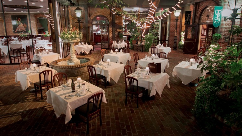 Outdoor courtyard with white tablecloth dining tables, fountain and lit up trees