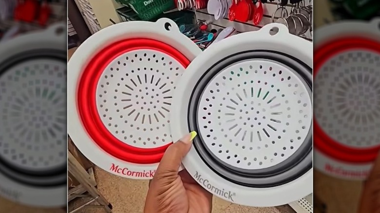 A hand holding two Dollar Tree McCormick collapsible colanders