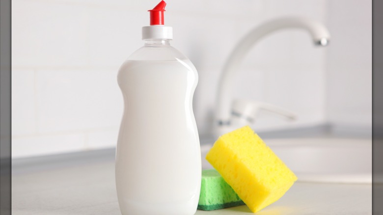 A bottle of dish soap next to sponges and a kitchen sink