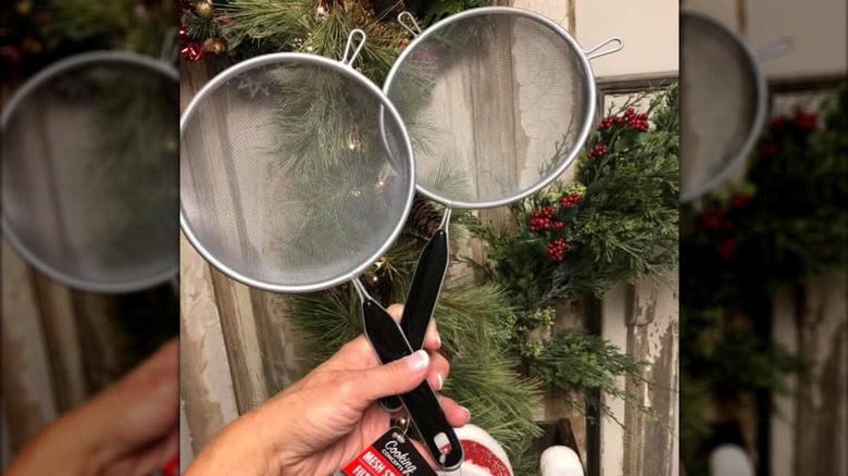 A hand holding two Dollar Tree mesh strainers