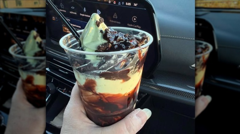A hand holding a Costco food court Double Chocolate Mint Sundae inside a car