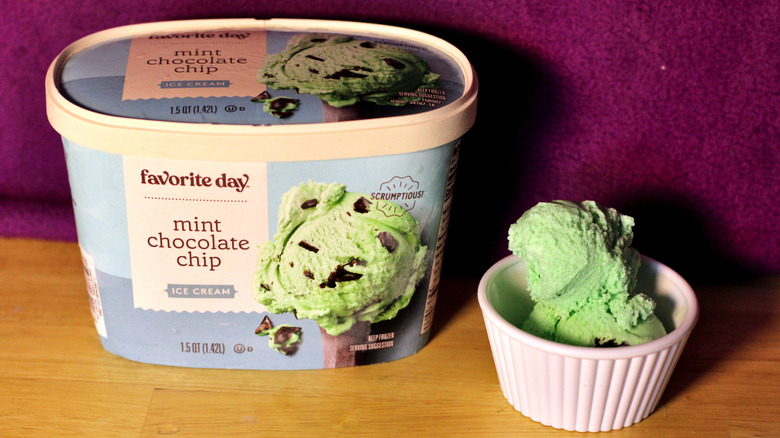 A container of Target's Favorite Day brand mint chocolate chip flavored ice cream beside a bowl of the scooped ice cream