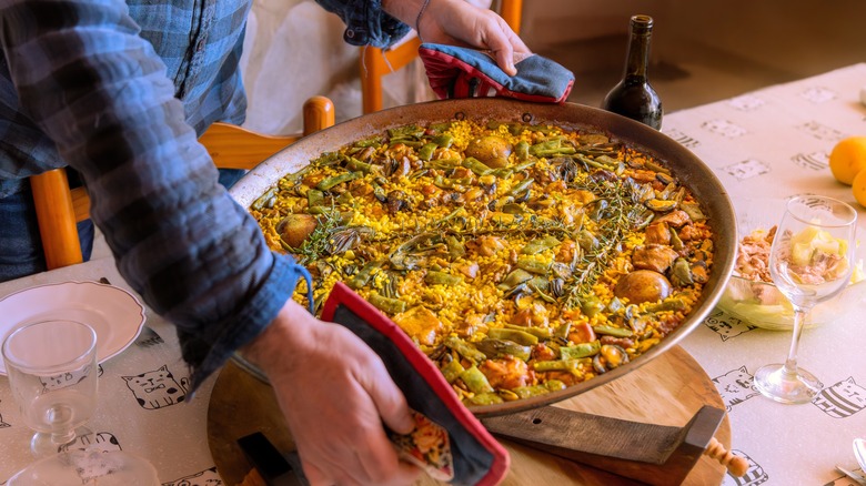 Hands placing dish of paella on table