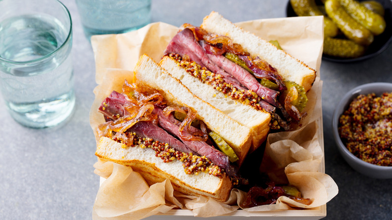 An overhead shot of a roast beef sandwich with caramelized onions, pickle, and mustard