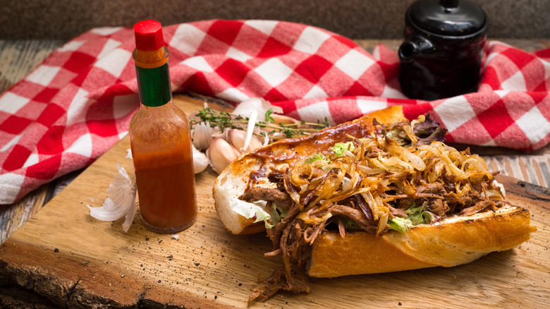 Debris poboy sandwich styled on a wood table with hot sauce and a dish towel