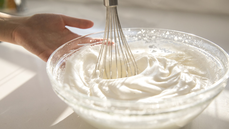 bowl of whipped cream with hand and whisk