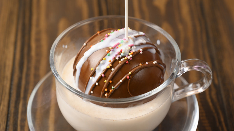 milk being poured over hot chocolate bomb in clear mug