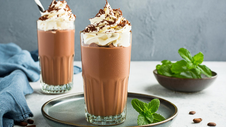 two chocolate milkshakes with whipped cream and fresh mint in background