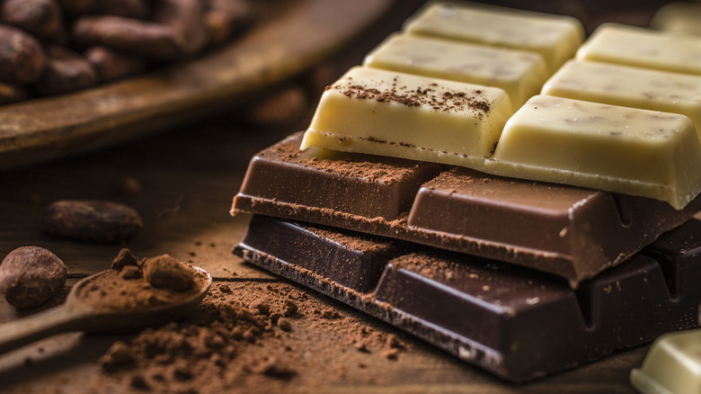 closeup of milk, white, and dark chocolate on wooden surface with cocoa beans