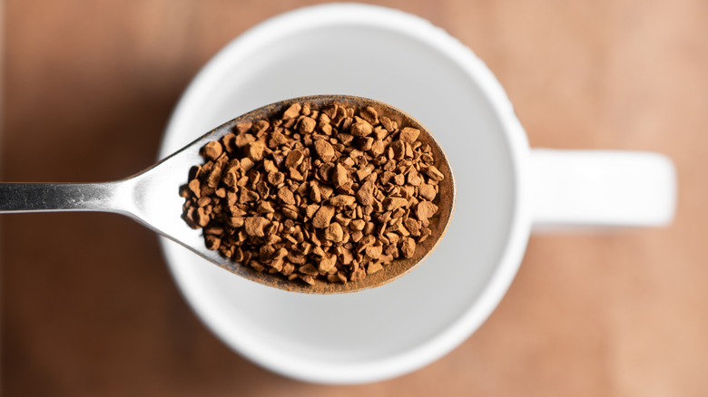Instant coffee in spoon over mug of water