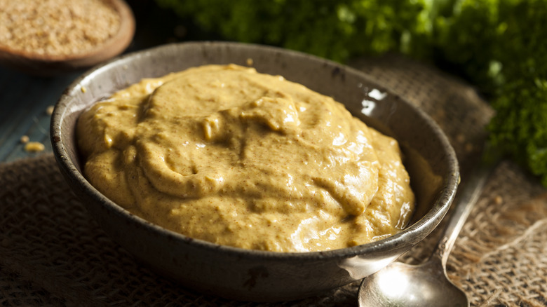 A bowl of brown mustard next to a spoon