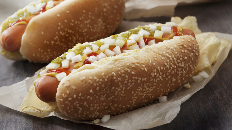 Two hot dogs topped with various toppings