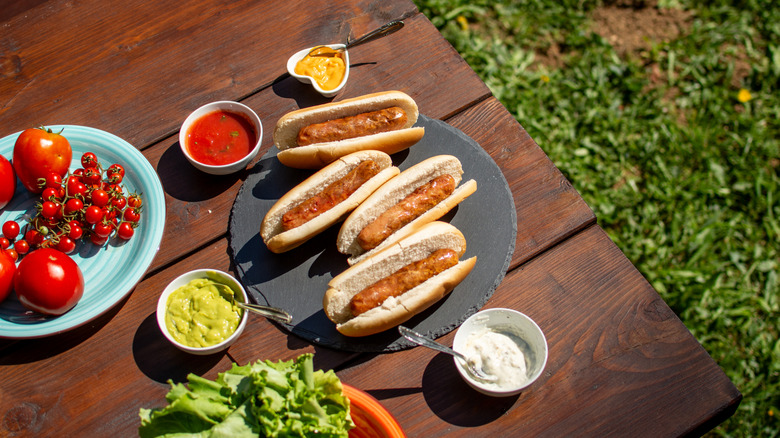 Hot dogs on a slate disc surrounded by various toppings