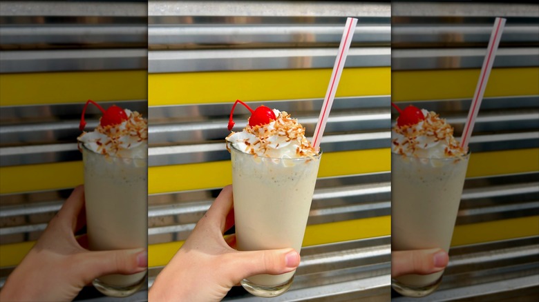 Hand holding milkshake in front of metal wall
