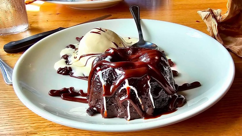 A hot fudge cake drizzled with frosting on a plate with ice cream
