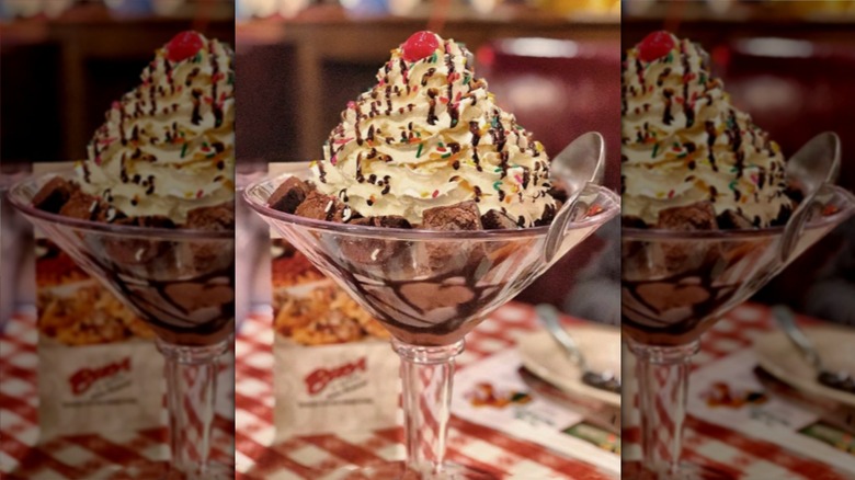 A Colossal Brownie Sundae heaped with whipped cream, sprinkles, and a cherry in a glass