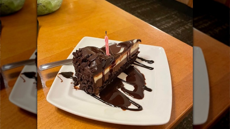 A slice of black tie mousse cake on a plate with a birthday candle in it