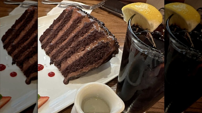 A slice of the Great Wall of Chocolate next to a glass of Coke with lemon