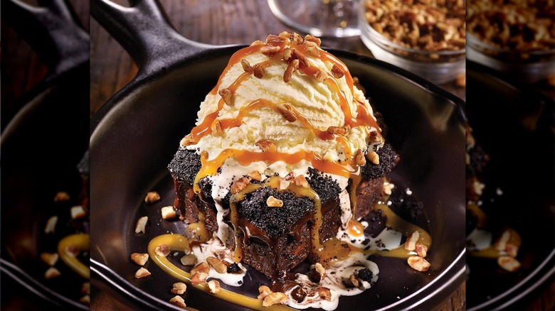 A chocolate brownie in a pot with a scoop of ice cream and nuts