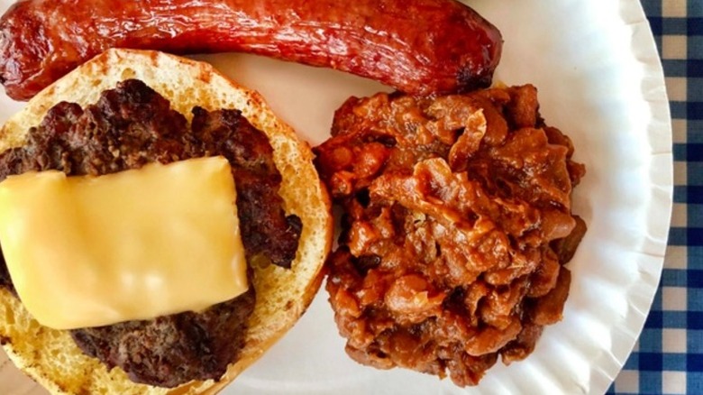 Paper plate with baked beans, sausage, and bread with meat and cheese