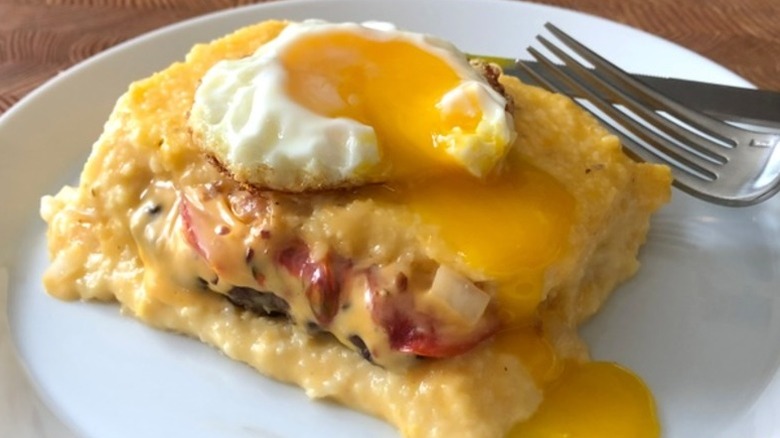 A slice of cheeseburger grits casserole with a fried egg on top on a plate