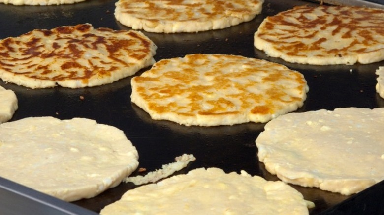 Rows of corn pancakes cooking on a griddle