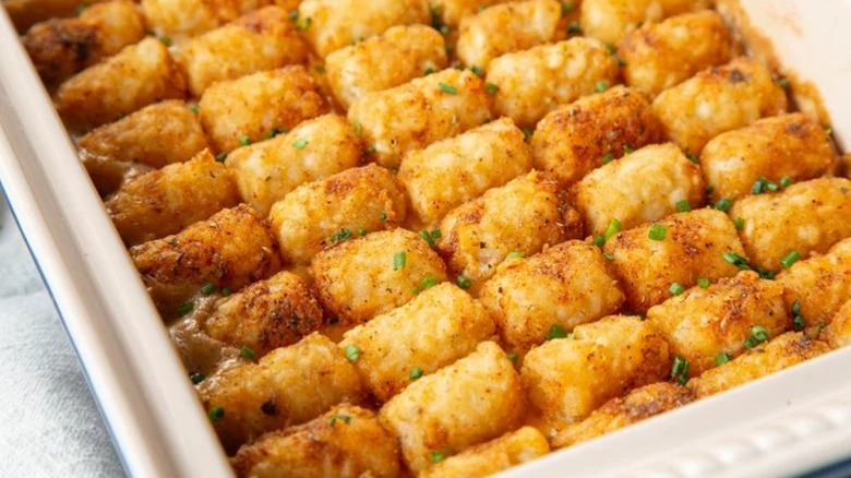 Tater tot casserole in a white casserole dish with chive garnish