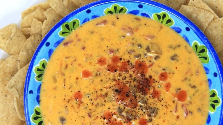 A colorful blue and green patterned bowl filled with green chile cheeseburger queso surrounded by tortilla chips