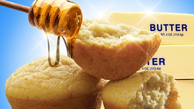 Corn muffins being drizzled with honey with butter sticks on a blue background