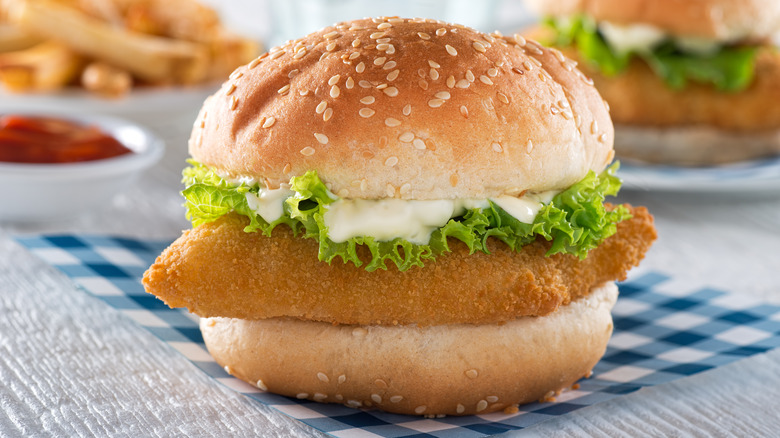 fried fish sandwich with lettuce and tartar sauce on blue checkered napkin