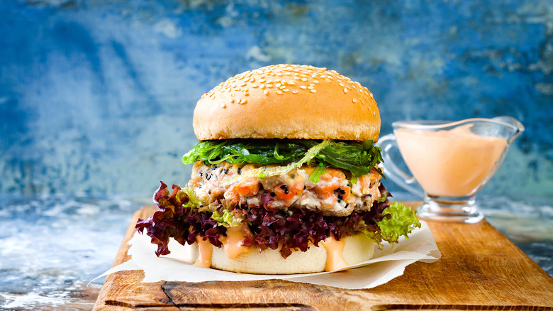 salmon burger with toppings and sriracha may in background