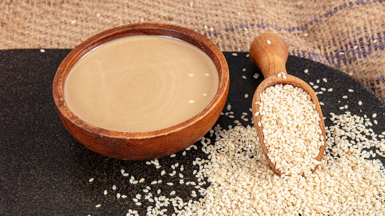wooden bowl of tahini next to sesame seed pile