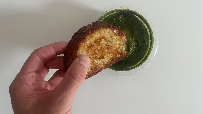 A hand dipping a piece of crusty bread into a Trader Joe's sauce