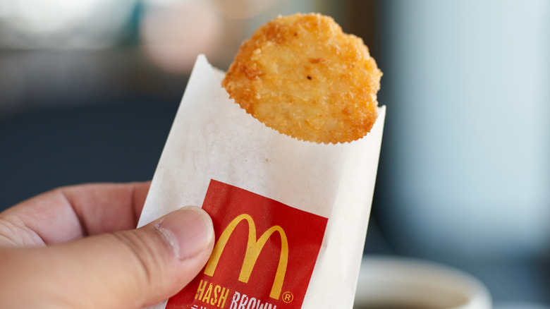 A hand holding a McDonald's hash brown in a paper sleeve