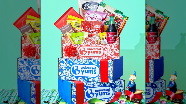 Three snack boxes from Universal Yums stacked on one another with the top box overflowing with assorted snacks