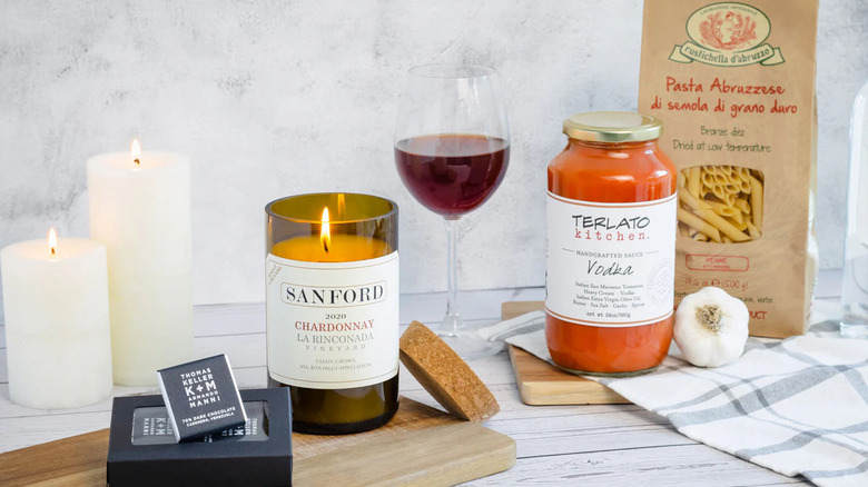 bag of pasta, candles, and vodka sauce from the Candlelight Dinner Gift Box on a wooden surface with glass of wine