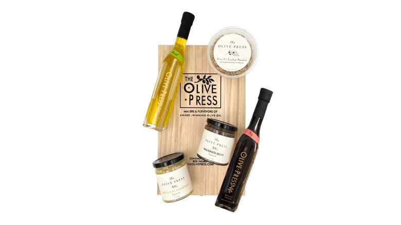 Celebrate gift set from The Olive Press featuring container of olives, a bottle of olive oil, a bottle of balsamic vinegar, and roasted almonds on a white background