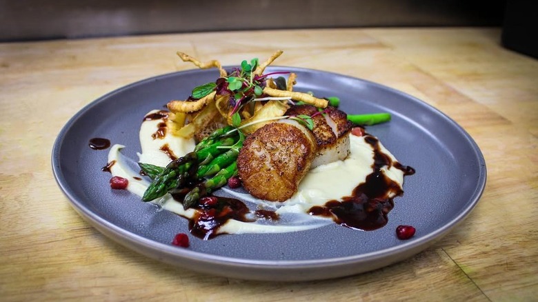 A blue plate of seared scallops and vegetables