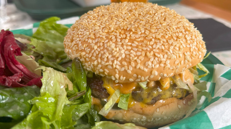 A burger with cheese on a sesame seed bun with salad