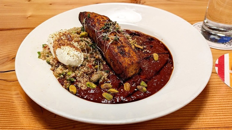 A fish entree on a plate with nuts and quinoa