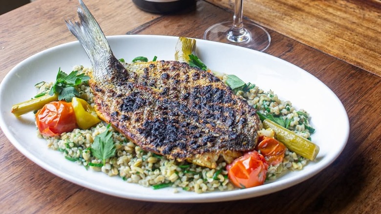 A cooked whole fish with fresh vegetables on a white plate