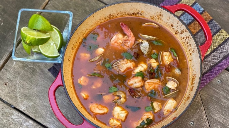 On a wooden table, a pot of seafood rice with prawns and mussels in a tomato gravy